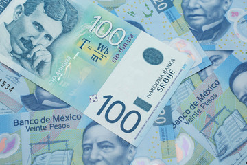A close up of a blue and white, one hundred Serbian dinar bank note on a background of Mexican twenty peso bank notes