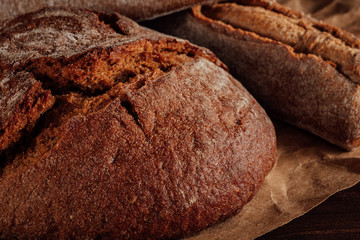 Rye bread with a crisp crust on paper lying on a wooden table. Illuminated by warm side sunlight. Concept for a bakery or for the bread Department in a store. Rustic style, warm brown tones, close-up.