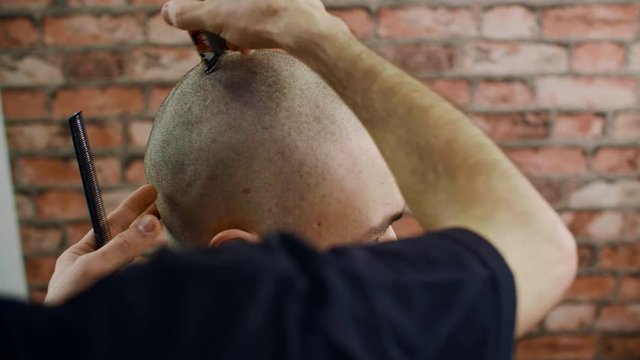 Male head shaving with trimmer in barbershop. Barber shaving bald male head with hair machine. Man getting shaving in barber salon