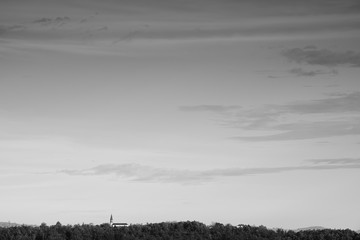 Black and white image of a distant church flanked by a lush forest line, Conques-Sur-Ciel, France