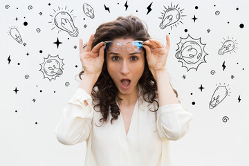 Pleasantly surprised woman taking off eyeglasses. Beautiful curly brunette holding spectacles and looking at camera with open mouth. Surprised concept