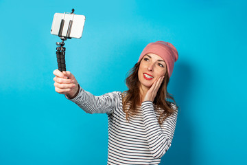 Young woman video blogger takes pictures of herself on the phone while broadcasting on a blue background. Concept story, vlog, selfie, blog