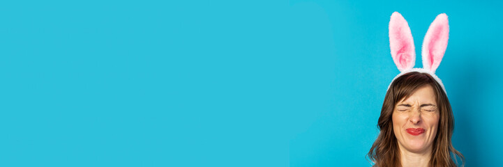 Young woman with closed eyes and ears of a rabbit on a blue background. Easter concept, surprise, hide and seek. Banner