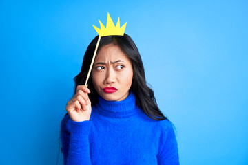 Young thoughtful woman with paper crown on stick looking away expressing doubt