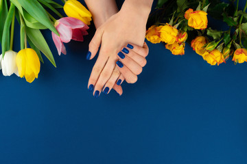 Obraz na płótnie Canvas Woman hands with manicure holding colorful tulips on blue background