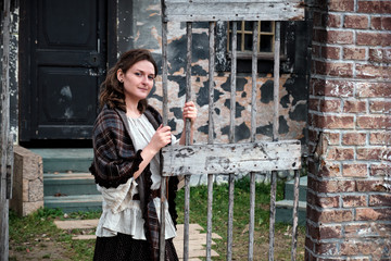Portrait of a brunette girl in the style of medieval Europe. A woman stands at the gate of an old house in retro clothes with flowers in her hands