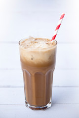 Ice coffee or caffe latte in a tall glass on a wood white background, Selective focus, copy space, Summer drink iced coffee.
