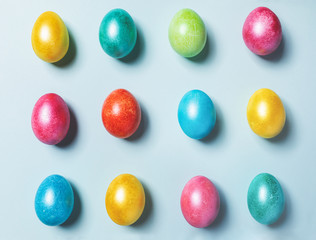 Easter composition of brightly multicolored painted glossy Easter eggs laid out on light blue pastel background.