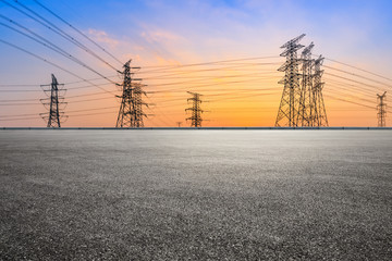 Fototapeta na wymiar Electricity tower silhouette and empty asphalt road at dusk