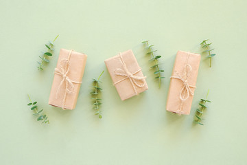 Three gift box wrapped in kraft paper, tied with jute twine and natural twigs of eucalyptus on green background. Holiday concept Copy space Top view Flat lay Template for your design