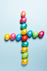 Easter creative composition. Colored glossy Easter eggs laid out in shape of cross on light blue pastel background.