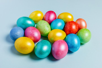 Fototapeta na wymiar Pile of colored glossy Easter eggs are lying on light blue pastel background.
