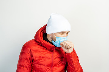young man with a medical mask on his face coughs on a light background. Concept of the common cold, virus, infectious diseases