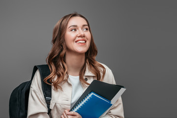 Happy girl student laughs and smiles and looking away holding a notebook isolated over dark grey background, copy space. University entrance exams concept