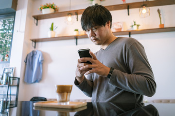 Attractive Asian man using smartphone to take coffee photos at the table in coffee shop. Film tone effected.