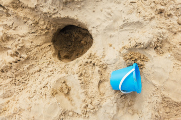 un seau en plastique bleu et un trou sur une plage de sable en été. Loisir d'enfant  © david