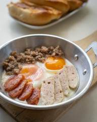 Fried eggs in a pan with meat on the wooden plate. The famous breakfast with Banh Mi - Vietnamese bun with meat.