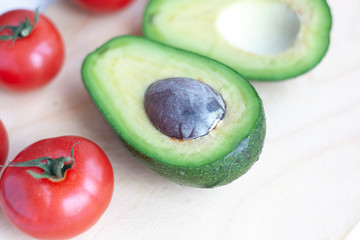 Ripe tomatoes and two halves of avocado on a wooden board