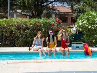 Three girls of different ethnicities with bathing suits of different colors toasting with beer in a pool and with a cassette