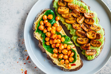 Vegan toasts with guacamole and mushrooms, hummus with chickpeas on rye bread, top view. Healthy vegan food concept.