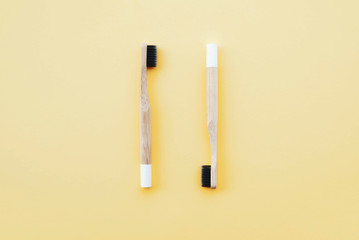 Stylish eco friendly natural bamboo toothbrushes on pastel yellow background.