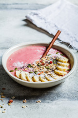 Berry smoothie bowl with granola, fruits and seeds in a white plate, gray background. Healthy vegan food concept.