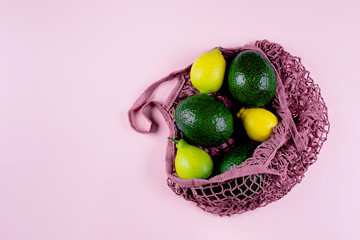 Mesh shopping bag with lemons and avocado on pink background. Top view, flat lay, copy space. Zero waste, eco friendly concept.