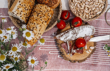 picnic in boho style. plaid on which lies a picnic food, sausages, nuts, red tomatoes and fresh buns. Composition, fresh air, juicy food. Natural light. top view