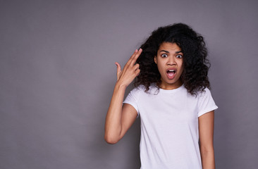 A young dark-skinned girl grimaces on a gray background.