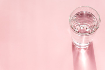 Close up of sparkling water in transparent glass and sun glare on pink background. Copy space for text