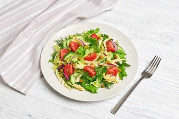Fresh salad with cherry tomatoes, savoy cabbage, cucumeber on dish. Healthy summer salad vegetarian meal concept. Tasty mixed leaves, tomatoes and mix vegetable salad on white wood