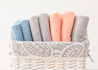 Comomposition of different colors terry towels folded in the white basket. Blue, gray and coral towels stacked in the white basket closeup photo