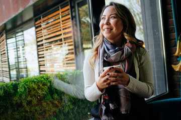 Beautiful Asian woman drinking coffee in warm cosy coffee shop and looking away	