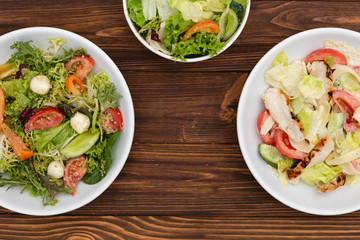 white deep plates with fresh salad ingredients mixed with sauce placed on a rustic background. A place for a menu, banner or advertisement