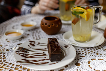 hands of the girl hold a transparent cup of tea with cinnamon, mint, orange on the table with a beautiful decor and dessert . warming fruit mint tea in the restaurant