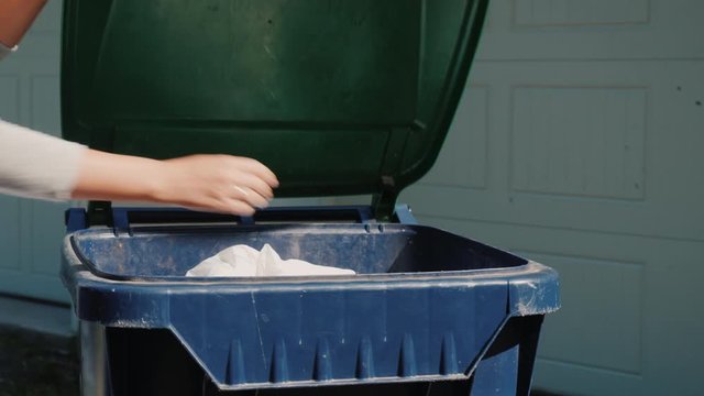 A bag of household waste is thrown into a plastic trash bin