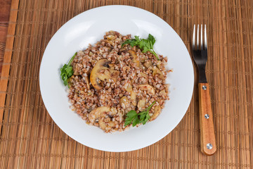 Buckwheat porridge with fried mushrooms and onions on dish, fork
