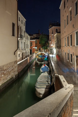 Narrow canal with boats and vintage houses at dusk. Venice city at night