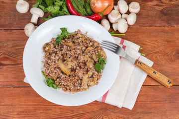 Buckwheat porridge with mushrooms on dish, fork, ingredients, top view