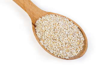 Raw barley groats in wooden spoon on a white background
