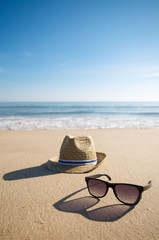 Simple summer hat and cool sunglasses casting long shadows in the setting sun on the smooth sand of an empty beach