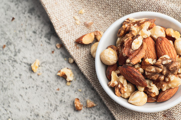Mixed nuts in white clean bowl on sack cloth contain walnuts, hazelnuts, almonds and macadamia. Healthy food and snack, diet food,  concept.