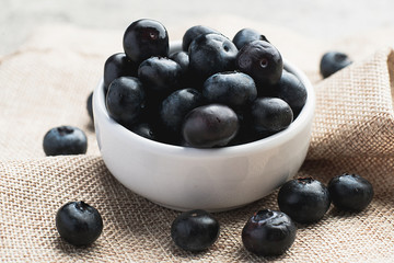 Fresh heap of blueberry in white clean bowl on sack cloth on minimal clean cement background. Healthy food, Fresh fruit, Vitamin and fiber source concept.