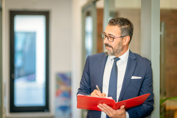 Fototapeta premium A charismatic, bespectacled bank employee takes notes on his red file