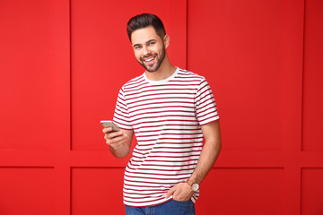 Handsome young man with mobile phone on color background