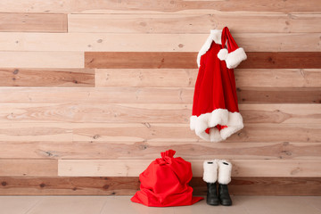 Santa Claus costume hanging on wooden wall near shoes and bag in room