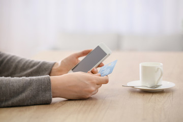 Woman using mobile phone for online banking at table
