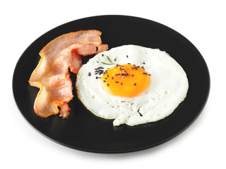 Plate with fried egg and bacon on white background