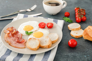 Plate with fried eggs, bacon and bread on dark background