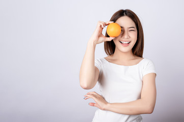 Beautiful young asian holding an orange with big smile in seamless white  isolated background. Diet healthy , beauty, fruit vitamin concept.